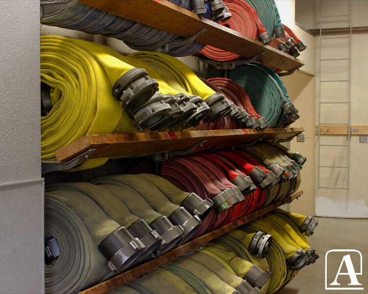 Coiled Amiflex firefighting hoses in various colors and coupling types stored in warehouse shelving, highlighting Amiflex hose quality and variety for industrial and firefighting use