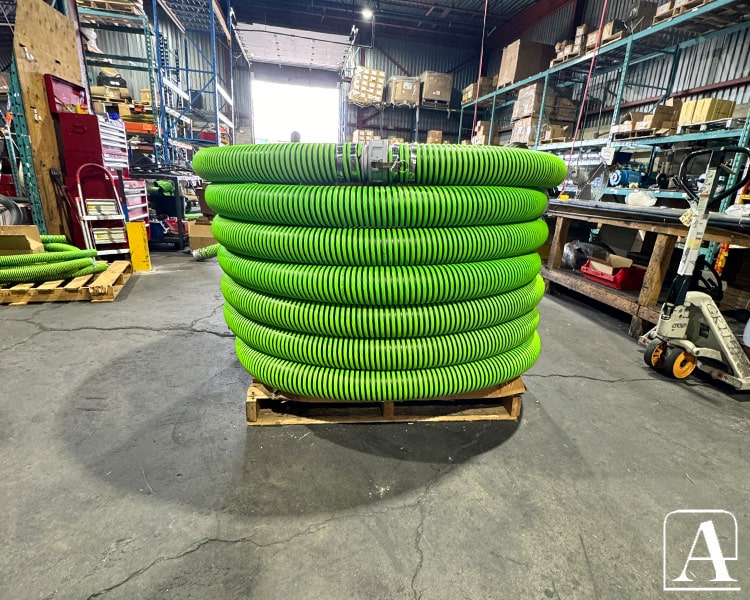 Multiple green Amiflex industrial hoses stacked in warehouse, emphasizing significant product stock and readiness for industrial deployment