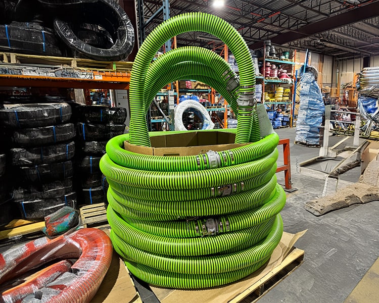 Stack of durable green Amiflex industrial hoses neatly organized in a warehouse, showcasing large inventory and heavy-duty hose solutions