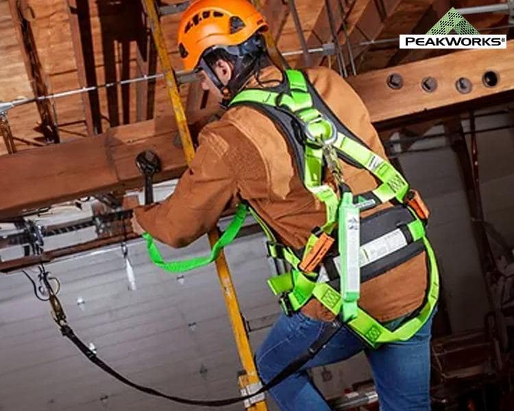 Construction worker in Peakworks safety helmet and harness, installing overhead equipment, highlighting workplace safety and industrial equipment