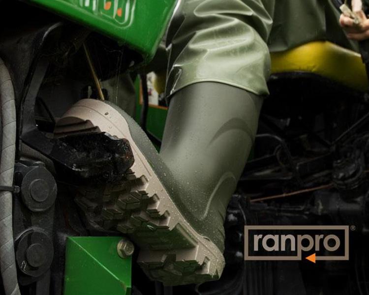 Close-up of a person wearing green rubber boots, operating a green agricultural machine, with Ranpro equipment visible. Ideal for agricultural machinery and farming tasks.