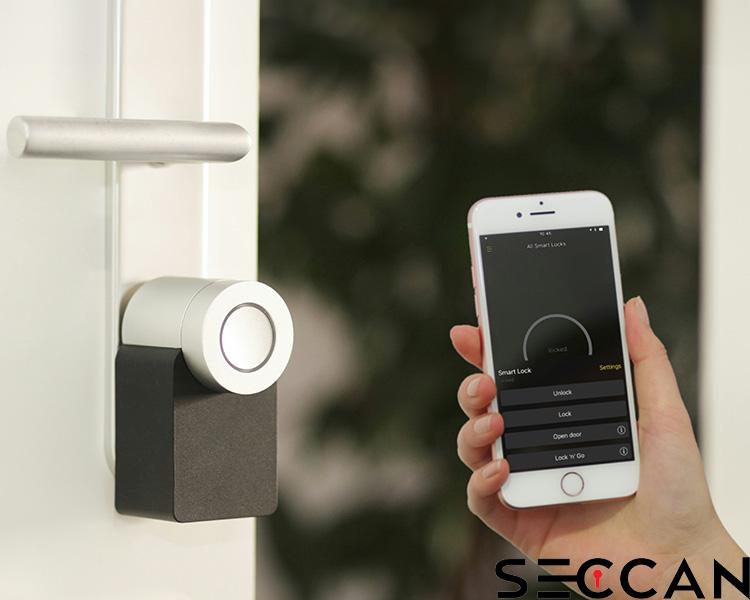 Hand holding a smartphone with Seccan smart lock app, controlling a Seccan lock mounted on a door, with options for locking and unlocking.