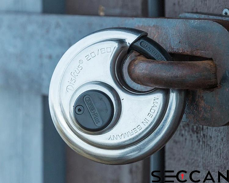 Weathered ABUS circular discus padlock secured in a metal latch with Seccan branding visible on textured wood.