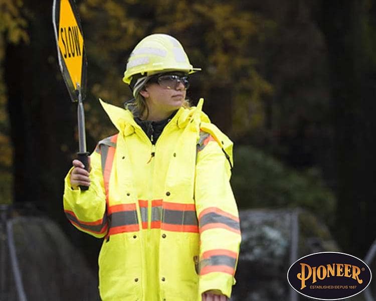 Woman wearing a Pioneer safety suit on a construction jobsite, holding a sign for site safety and awareness.